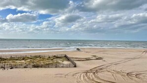 Una playa con una valla de madera, terreno arenoso y cielo nublado.