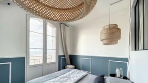 Un dormitorio con cama, ventana, lámpara colgante y vista al exterior.
