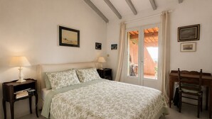 Un dormitorio con cama, dos mesitas de noche, un escritorio, una silla y un ventanal con cortinas.