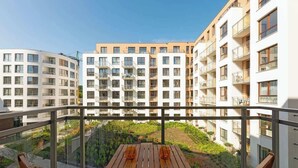 Een balkon met een houten tafel en stoelen, met uitzicht op een tuin en omliggende gebouwen.