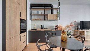 Een moderne keuken met houten kastjes, een zwart aanrecht en een eethoek met een ronde tafel en stoelen.