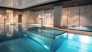 Une piscine intérieure moderne, dotée d’une eau cristalline, de parois en verre et d’un design minimaliste.