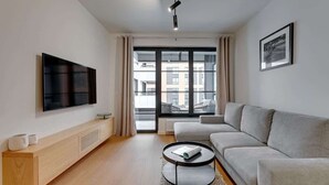 A modern living room with a flat-screen TV, a sofa, a coffee table, and a window with a view of buildings.