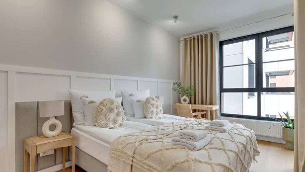 A bedroom with a bed, bedside table, lamp, and a window with curtains.