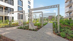A modern outdoor area with a paved walkway, metal pergolas, and seating areas. - Doki A34 B | Gdańsk Shipyard & Foodhall (Gdańsk)