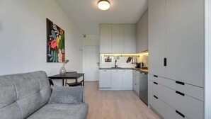 A modern living room with a grey sofa, a small table with a vase, and a colorful abstract painting on the wall. - Doki A34 B | Gdańsk Shipyard & Foodhall (Gdańsk)