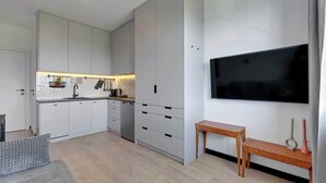 A modern kitchen with white cabinets, a built-in oven, and a large flat-screen TV mounted on the wall. - Doki A34 B | Gdańsk Shipyard & Foodhall (Gdańsk)