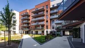 Un immeuble résidentiel à plusieurs étages, doté de balcons, d’une cour pavée et d’un petit jardin.
