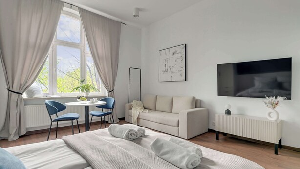 A modern hotel room with a bed, a sofa, a TV, a desk with chairs, and a window with curtains. - Chopina Studio | 300 metres to the Sopot beach (Sopot)