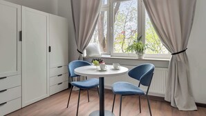A room with a white table, two blue chairs, a white cabinet, and a window with curtains. - Chopina Studio | 300 metres to the Sopot beach (Sopot)