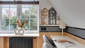 Et moderne værelse med et stort vindue, en radiator, et bord med lampe og et billede af bygninger på væggen.
