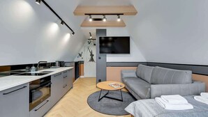 Et moderne køkken med indbygget ovn, et spiseområde med et rundt bord, en grå sofa og et fladskærms-tv på væggen.