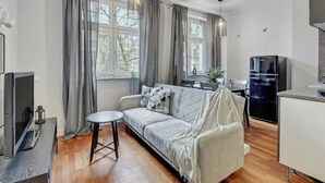 Ein modernes Wohnzimmer mit einer Couch, einem kleinen runden Tisch, einem Fernseher und einer Küchenzeile mit einem Kühlschrank.
