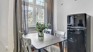 Eine moderne Küche mit einem schwarzen Amica-Kühlschrank, einem Esstisch mit Stühlen und einem Fenster mit Vorhängen.