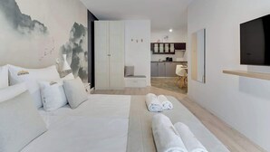 Habitación de hotel con cama, escritorio, silla, televisor y vista a la cocina.