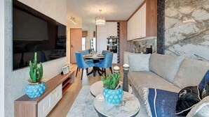 Ein modernes Wohnzimmer mit Sofa, Couchtisch und Fernseher. Es gibt eine Essecke mit Stühlen und einem Tisch.