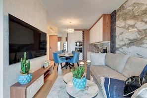 Ein modernes Wohnzimmer mit Sofa, Couchtisch und Fernseher. Es gibt eine Essecke mit Stühlen und einem Tisch.