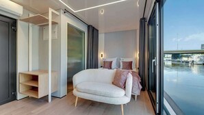 A modern bedroom with a sofa bed, a built-in shelf, and a view of the water.