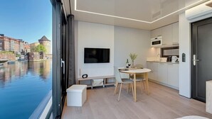 A modern room with a TV, dining table, and kitchen area, overlooking a canal with historic buildings.
