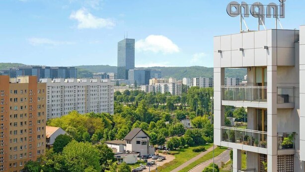 En modern byggnad med en skylt där det står ”onani” och utsikt över en stadsbild med olika byggnader och grönska.