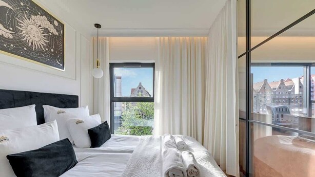 Et hotelværelse med en stor seng, udsigt til bygninger og en balkon.