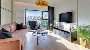 En moderne stue med en sofa, et rundt sofabord, et fjernsyn og et stort vindue med udsigt over byen.