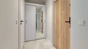 A hallway with a mirrored closet door, a wooden door, and a light switch on the wall. - Chłopska 2 | Near the Beach (Gdańsk)