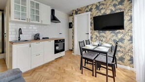 Une cuisine compacte avec des meubles blancs, une hotte noire et un coin repas comprenant une table et des chaises.