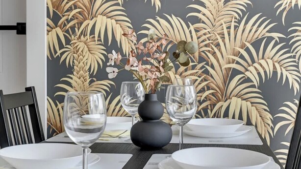 Une table à manger dressée avec de l’assiette blanche, des verres à vin transparents et un vase rempli de fleurs.