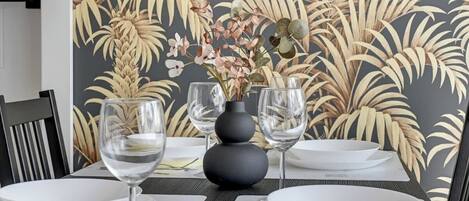 A dining table set with white plates, clear wine glasses, and a vase with flowers.