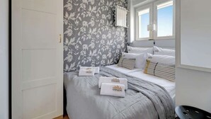 Une chambre à coucher avec un lit, des oreillers, une table de chevet, une lampe et une fenêtre.