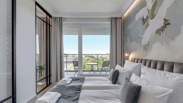 A hotel room with a large bed, a balcony with a view, and a mural on the wall. - Gdynia Modern Tower | Great City View | 13 floor (Gdynia)