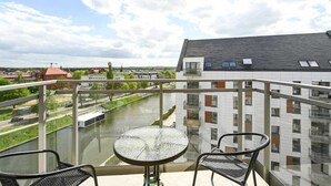 Een balkon met een glazen tafel en stoelen, met uitzicht op een rivier en gebouwen.