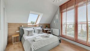 Een moderne slaapkamer met een schuine kap, dakraam, een bed met witte beddengoed, een klein nachtkastje en uitzicht door grote ramen.
