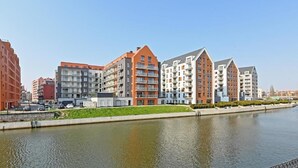 A modern urban waterfront with multi-story residential buildings, a canal, and a clear sky. - Aura Island 66 | Riverside | City Center & Parking (Gdańsk)