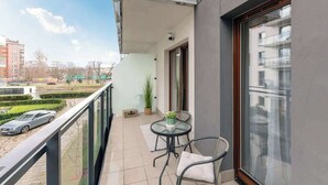 A balcony with a table and chairs, a potted plant, and a view of the street. - Aura Island 66 | Riverside | City Center & Parking (Gdańsk)