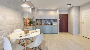 A modern kitchen with light wood cabinets, a central island, and a dining area with white chairs and a table. - Aura Island 66 | Riverside | City Center & Parking (Gdańsk)