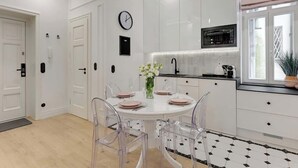 A modern kitchen with white cabinetry, a round dining table with clear chairs, a clock on the wall, and a microwave above the counter. - 500 metres to the Sopot Beach | Monte Cassino (Sopot)