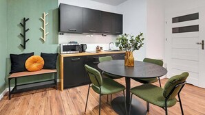 A compact kitchen with dark cabinets, a microwave, and a coffee maker. There is a round table with green chairs and a bench with black cushions. - Aura 196B | Riverside | City Center (Gdańsk)