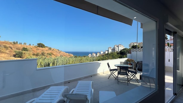 Ein Balkon mit Tisch und St ühlen mit Blick auf eine Küstenlandschaft mit Gebäuden und Vegetation.