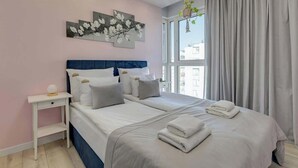 A double bed with white bedding and a headboard, a bedside table with a lamp, and a large window with curtains. - Letnica 147 with Balcony | Seaside (Gdańsk)