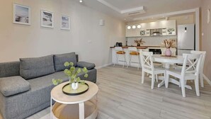 A modern living room with a grey sofa, a round coffee table, and a dining area with white chairs and a small table. - Letnica 147 with Balcony | Seaside (Gdańsk)