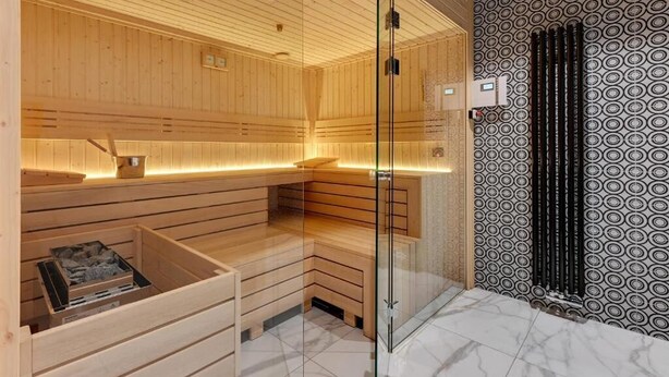A sauna with wooden benches, a glass partition, and a patterned wall.