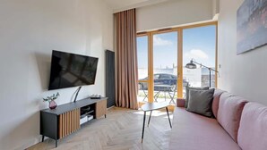 Ein modernes Wohnzimmer mit einem Flachbildfernseher, einer Couch, einem Couchtisch und Blick durch große Fenster nach draußen.