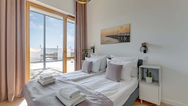 Ein modernes Hotelzimmer mit einem großen Bett, einem Nachttisch, einer Zimmerpflanze und einem Gemälde eines Piers.