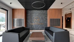 Eine moderne Lobby mit zwei schwarzen Sofas, einem Holztisch und einer Marmorwand mit einem Logo.