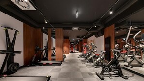 Ein Fitnessraum mit Laufbändern, Crosstrainern und Krafttrainingsgeräten, die in Reihen angeordnet sind.