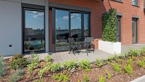 Ein modernes Gebäude mit großen Glasfenstern, einer Ziegelaußenwand und einer Terrasse mit Gartenmöbeln.