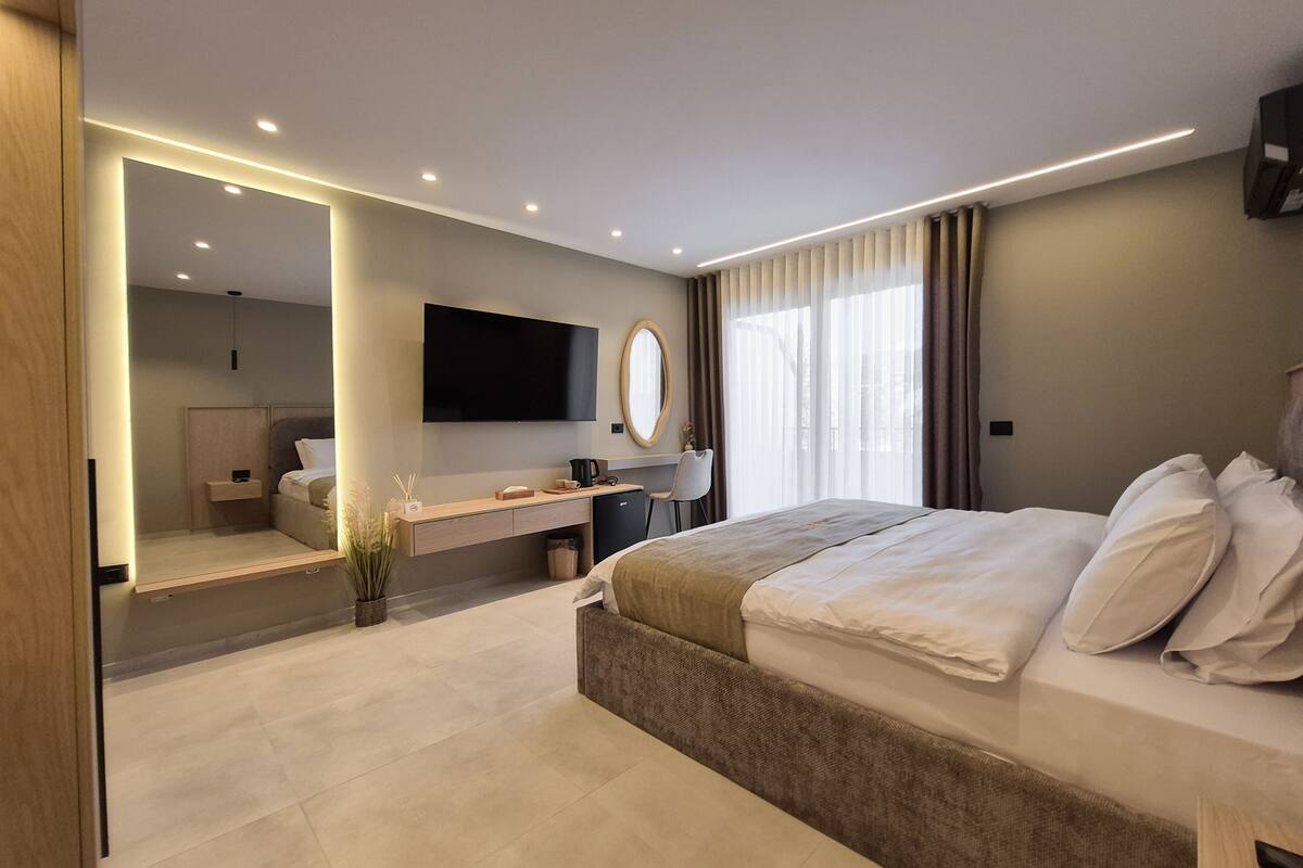 A modern hotel room with a large bed, a desk, a flat-screen TV, and a large mirror.