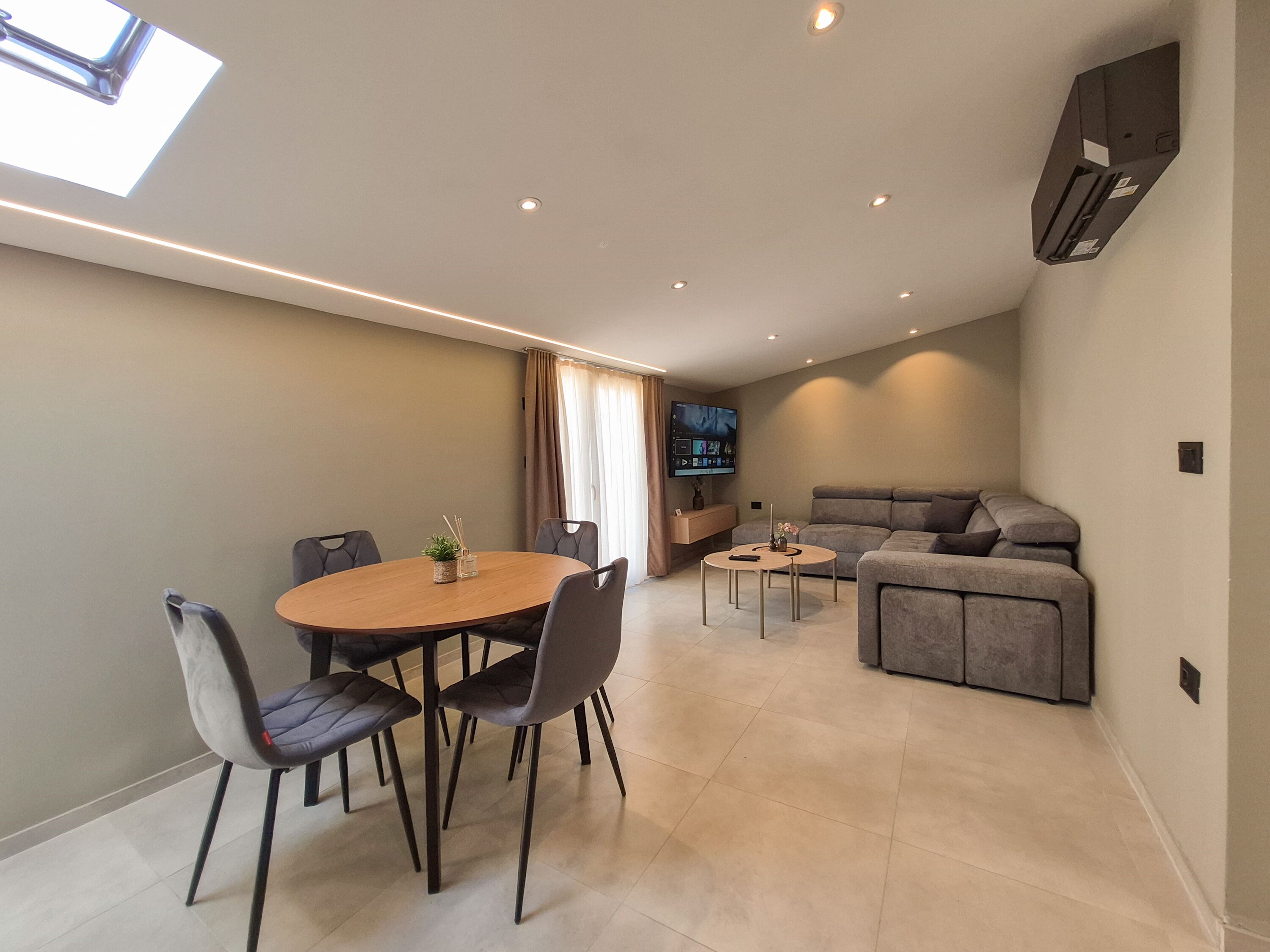 A modern living space with a dining area, a sofa, a TV, and a skylight.